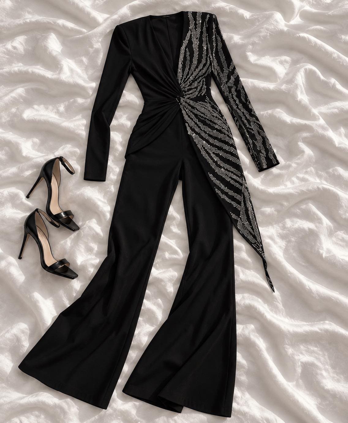 Black sequined jumpsuit with flared legs and black high heels on white fabric.