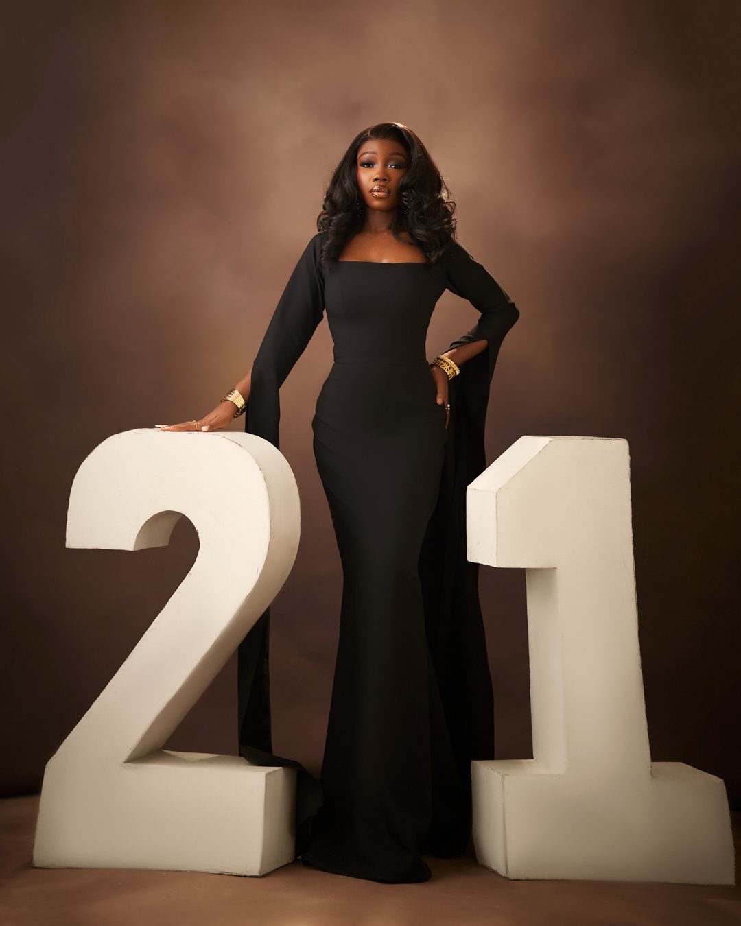 A woman in a black evening gown posing between large white numbers twenty-one.