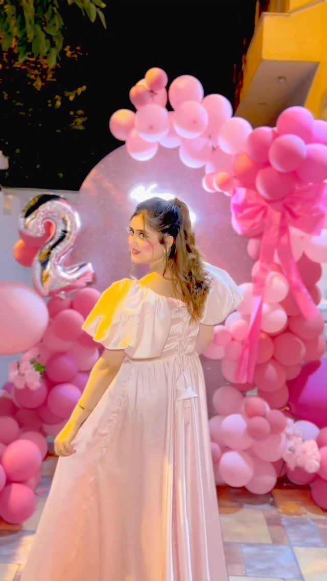 Woman in a pink puff-sleeve dress posing against a pink balloon arch.