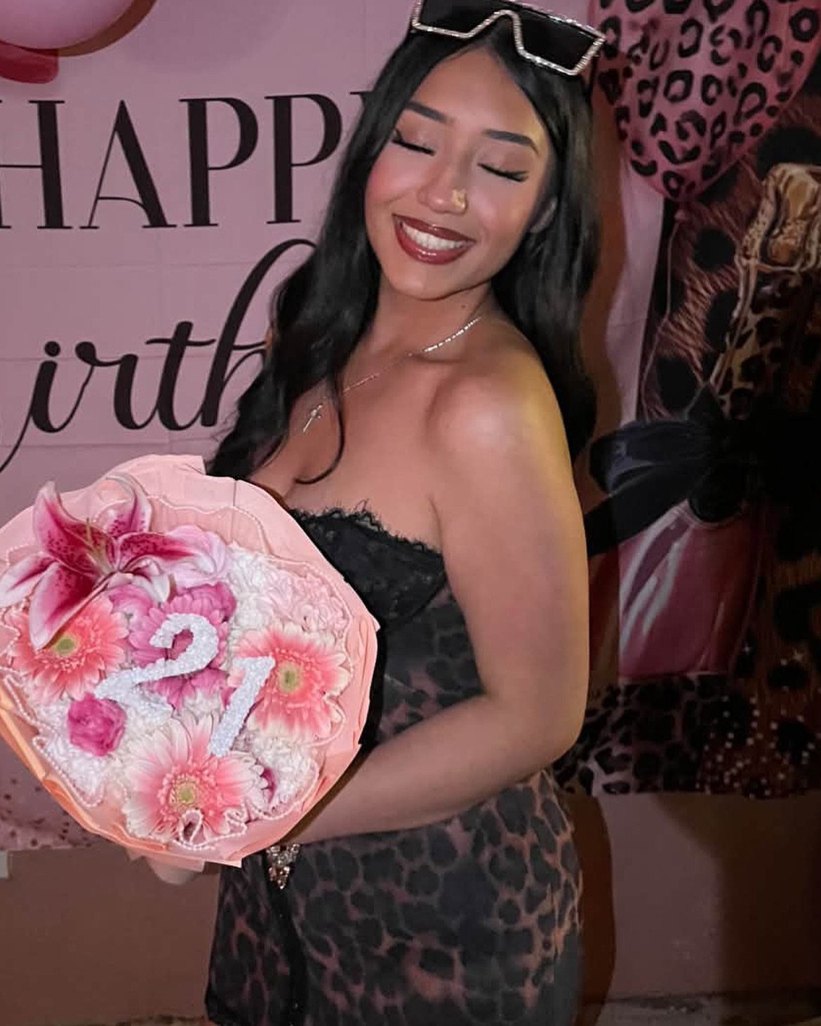 Smiling woman in leopard print dress holding a pink flower bouquet with a glittery number 21.
