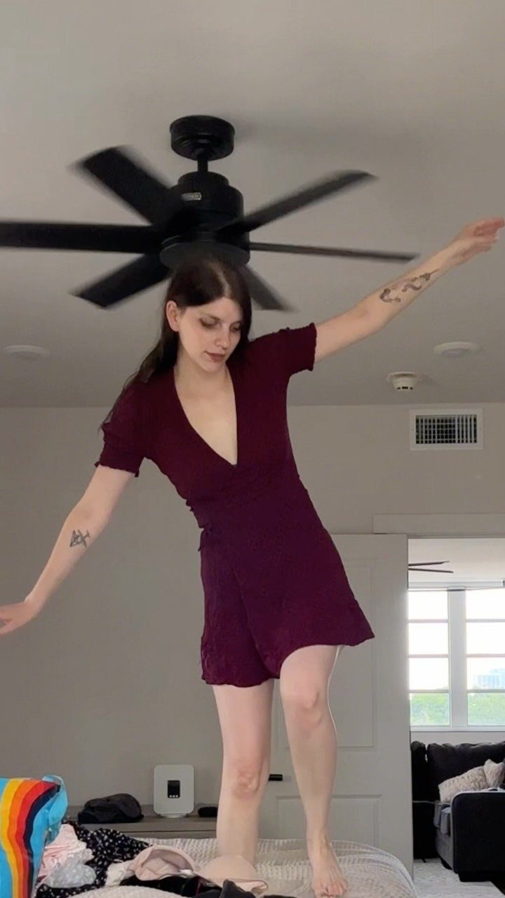 A woman in a maroon V-neck wrap dress posing with arms outstretched in a room.