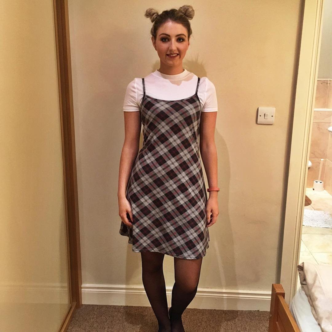 A woman wearing a plaid slip dress over a white t-shirt and black tights.