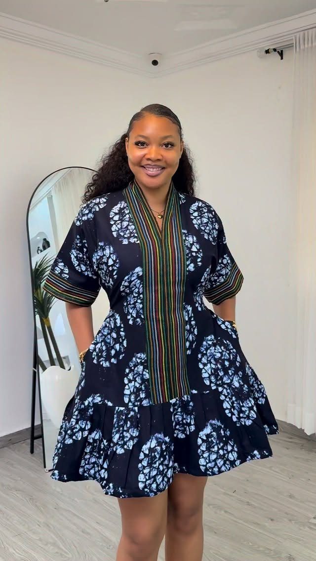 A smiling woman wearing a short, patterned blue casual African attire dress with striped details.