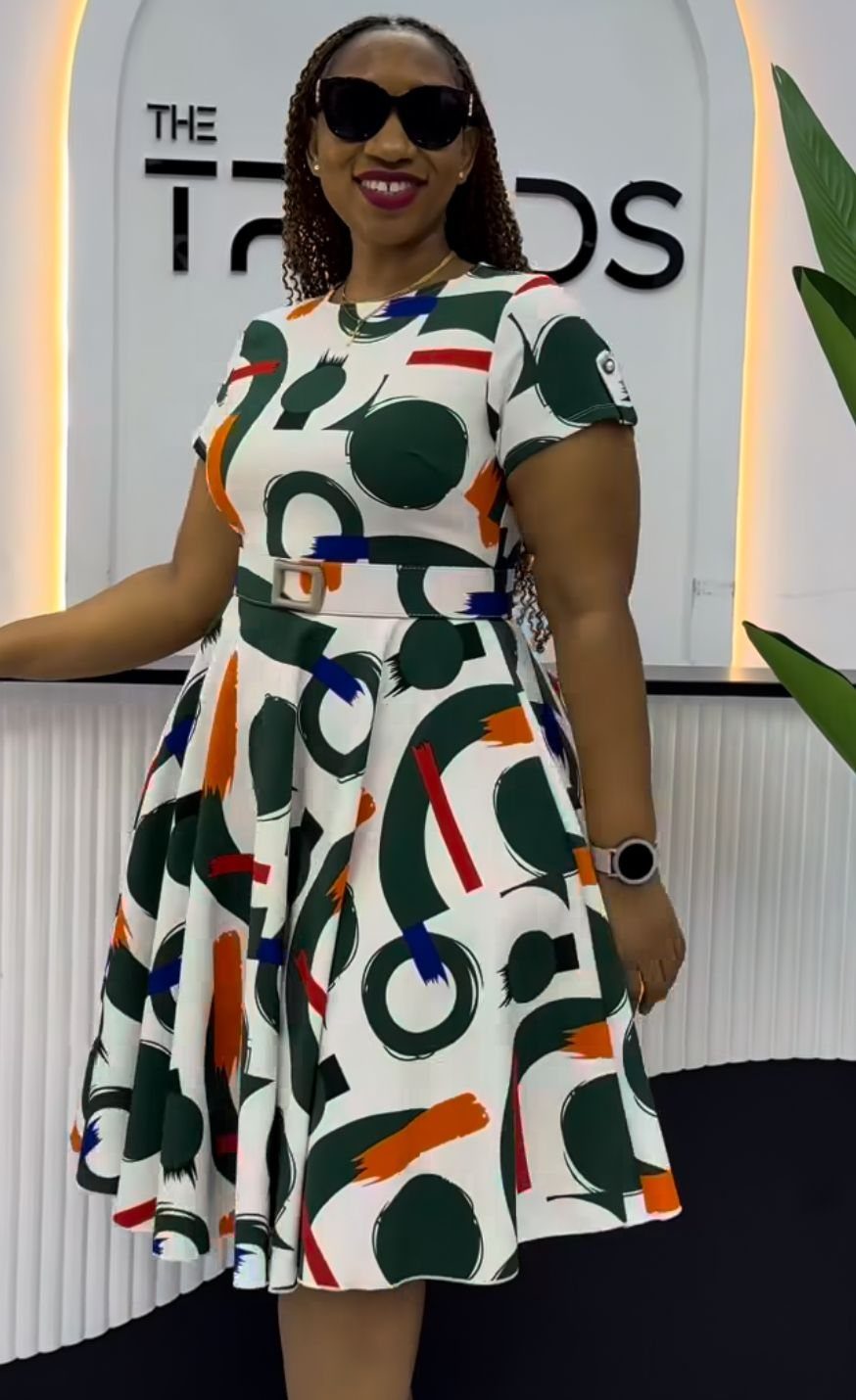A woman smiling in a patterned white flared dress with a cinched waist and short sleeves.