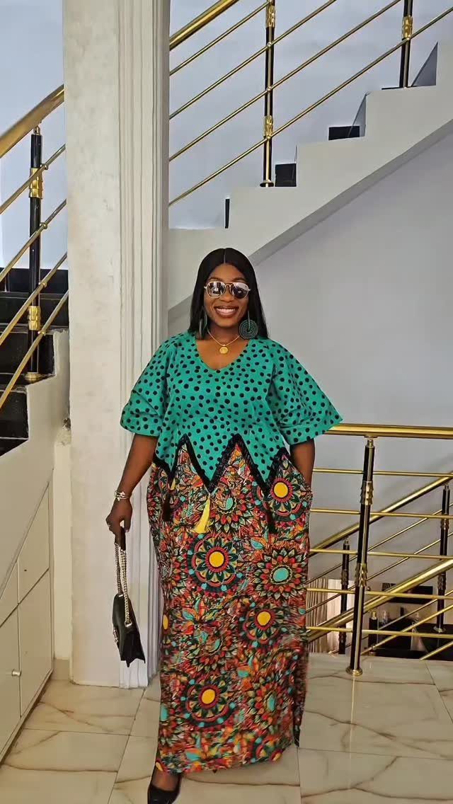 A smiling woman posing in a teal and patterned plus-size African flared sleeve dress.