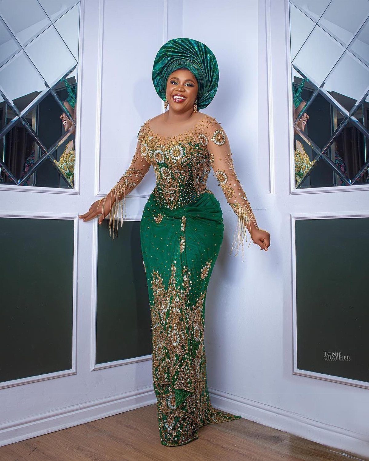 Woman in a formal green and gold embroidered mermaid gown with a matching headwrap.
