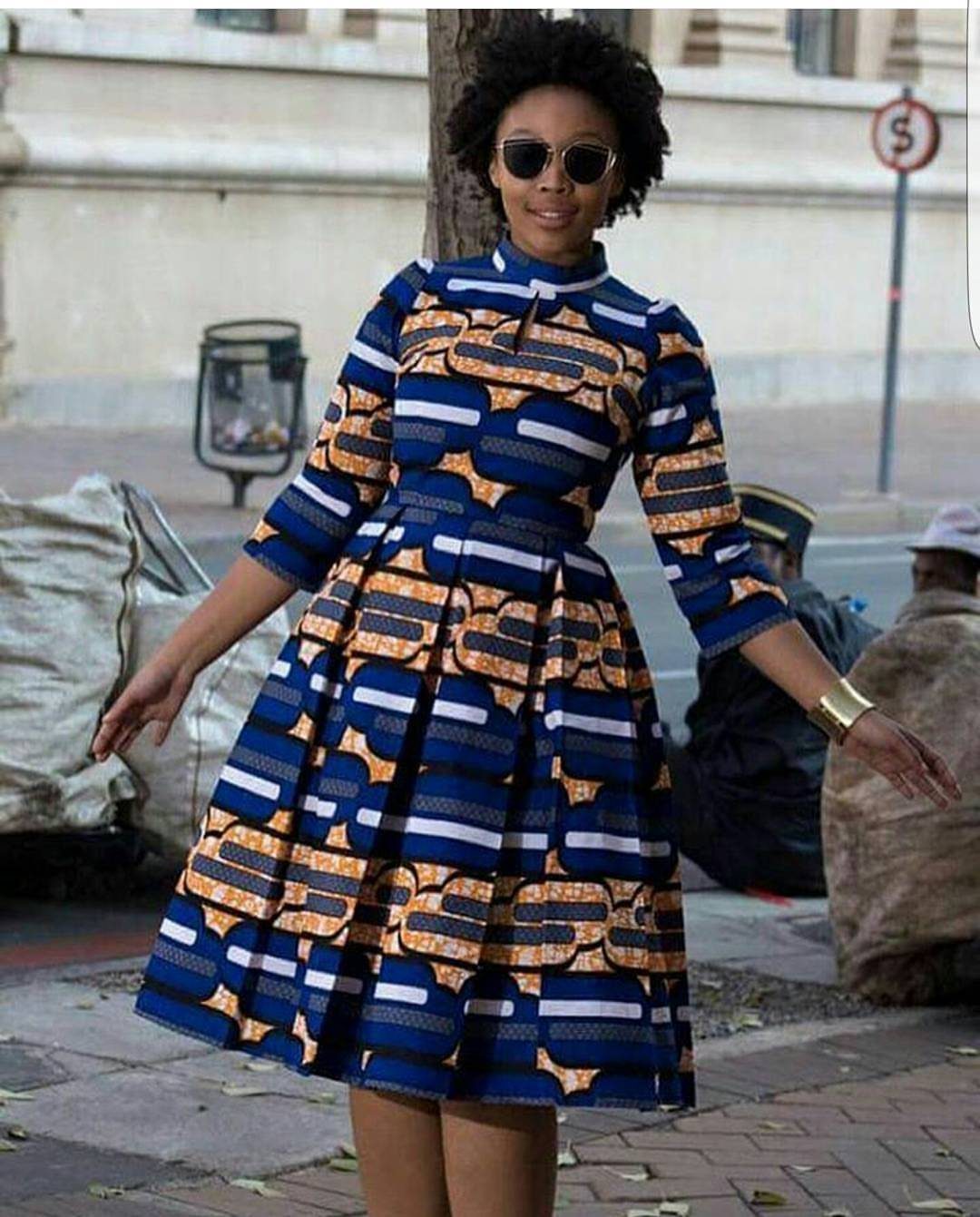 A woman wearing a colorful blue and orange patterned Kitenge dress posing outdoors.
