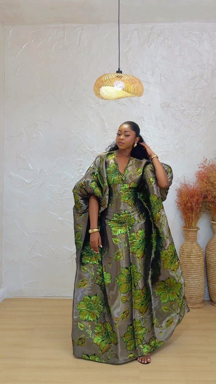 A woman wearing a long, shimmering green and grey floral maxi dress with flared sleeves.