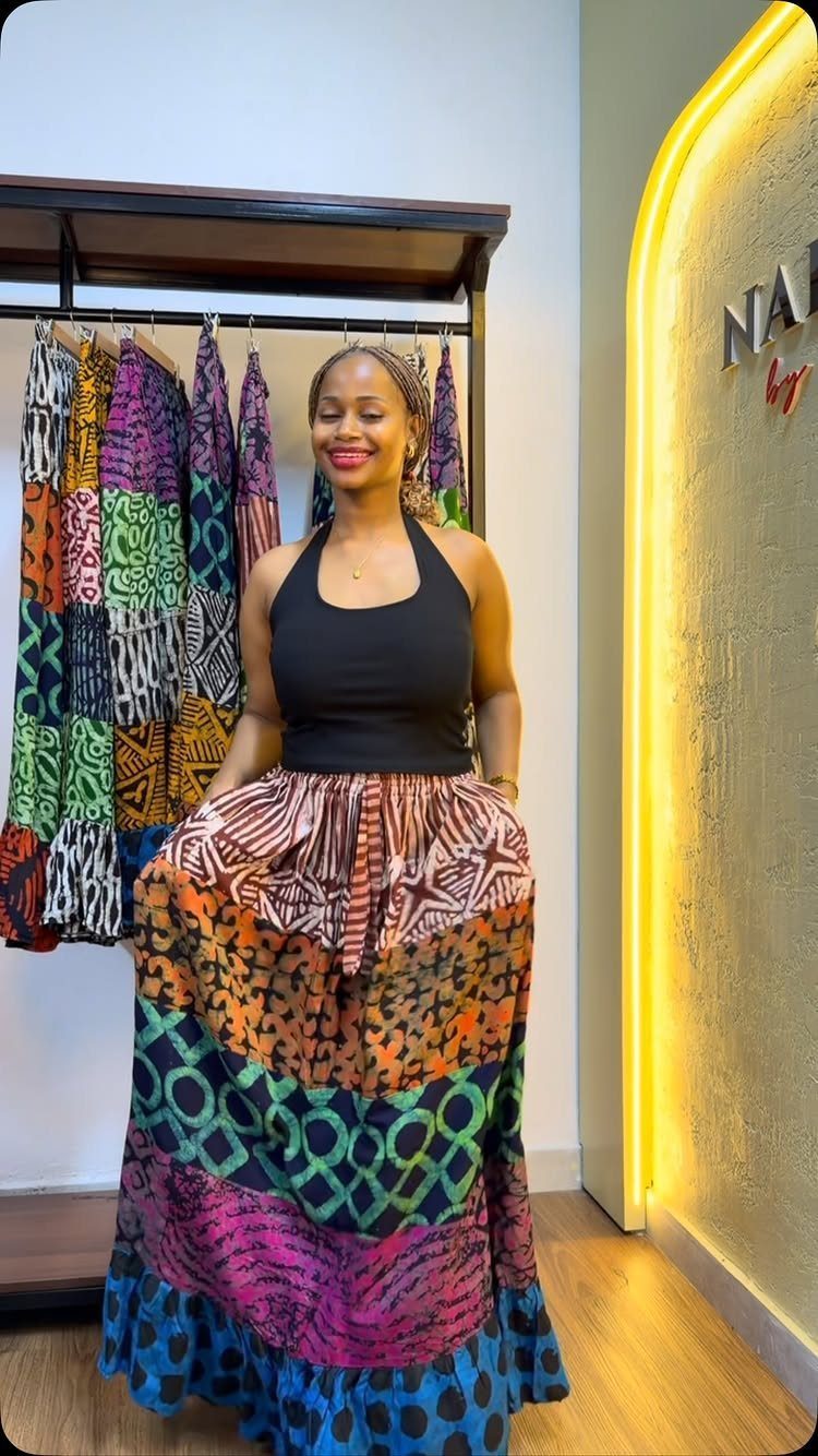 A smiling woman wearing a colorful patterned African print maxi skirt and black halter top.