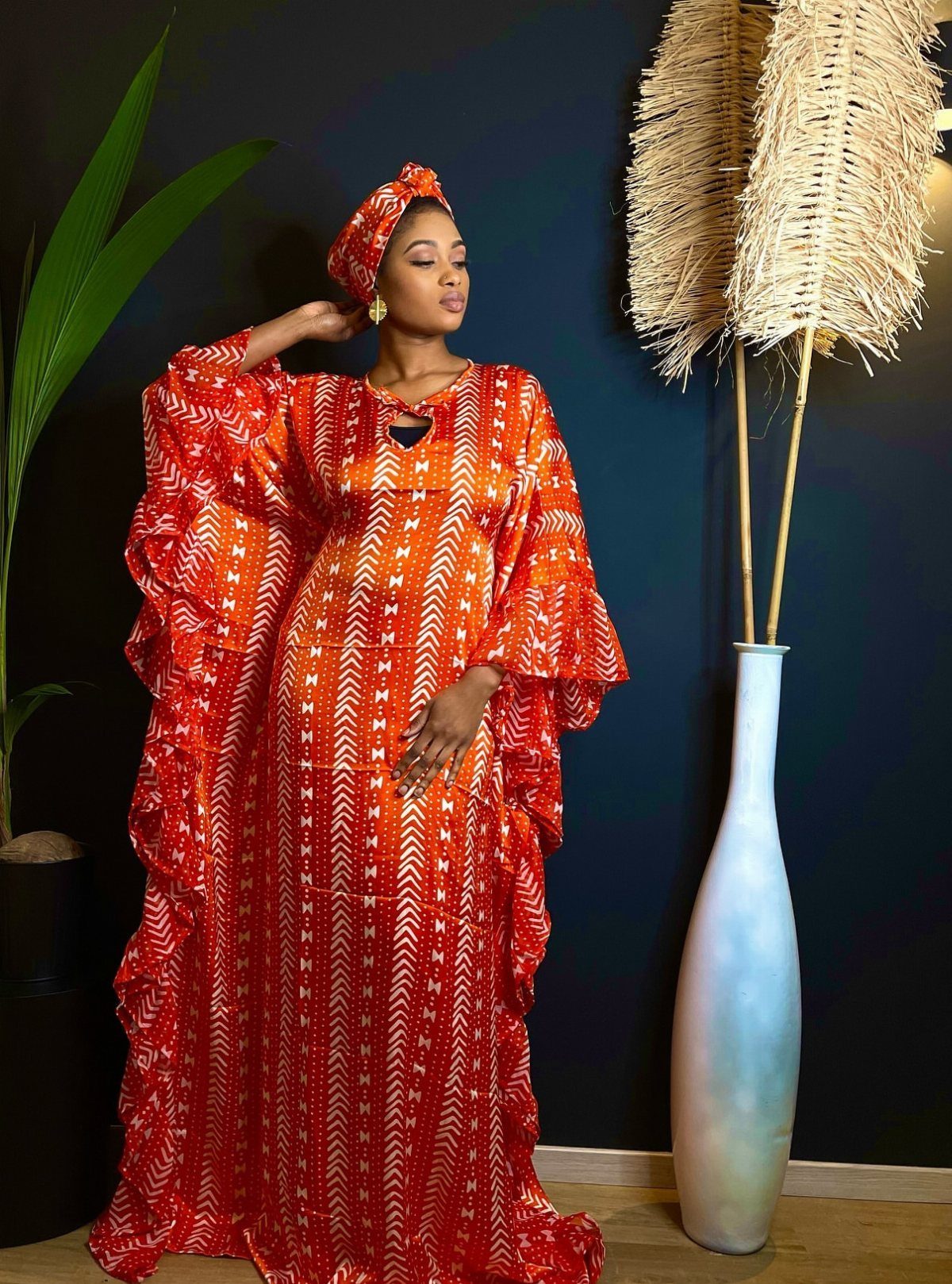 Woman in a red patterned African wax print dress and matching headwrap posing indoors.