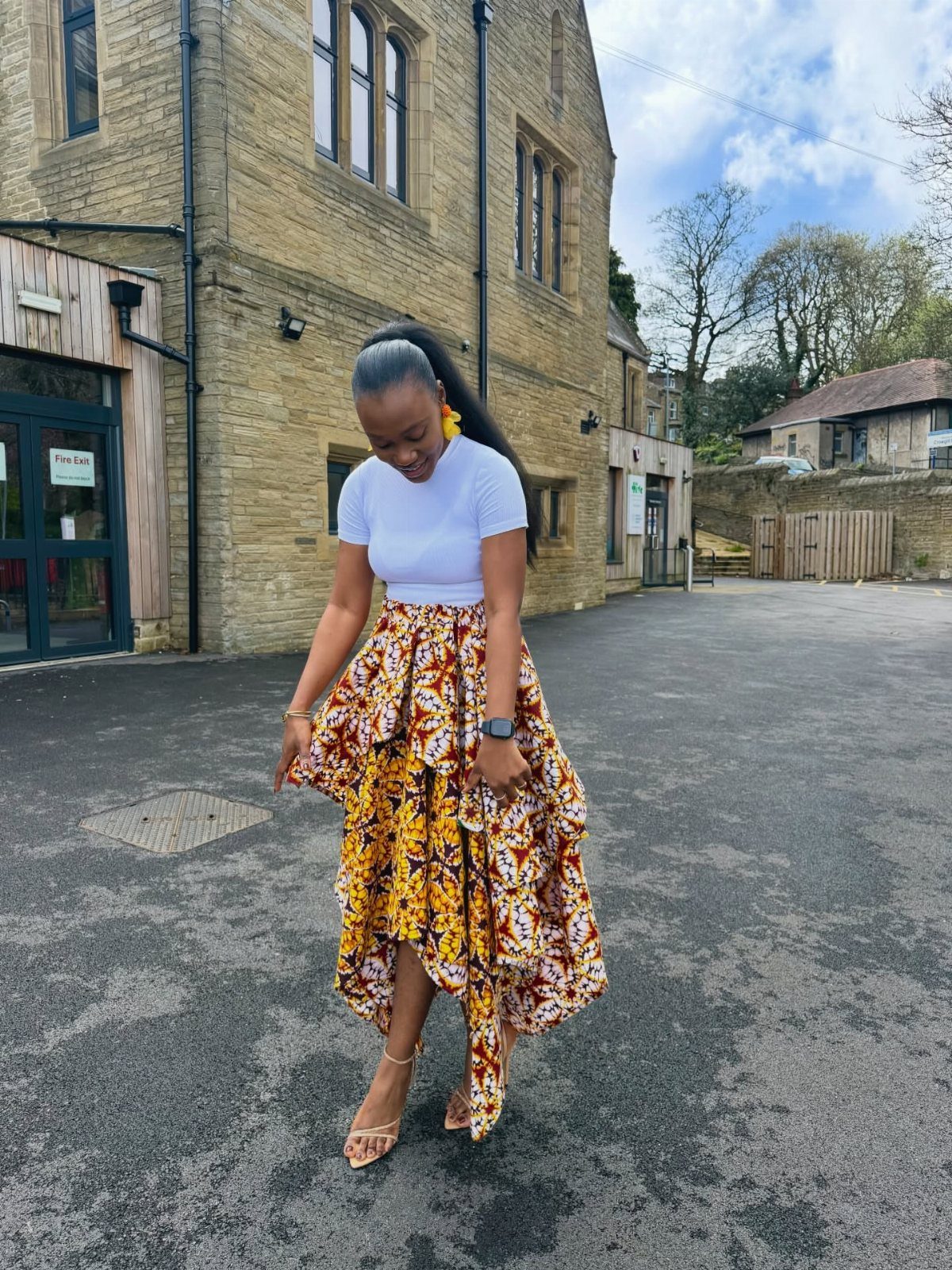A woman wearing a vibrant yellow and brown patterned layered asymmetrical skirt and white t-shirt.