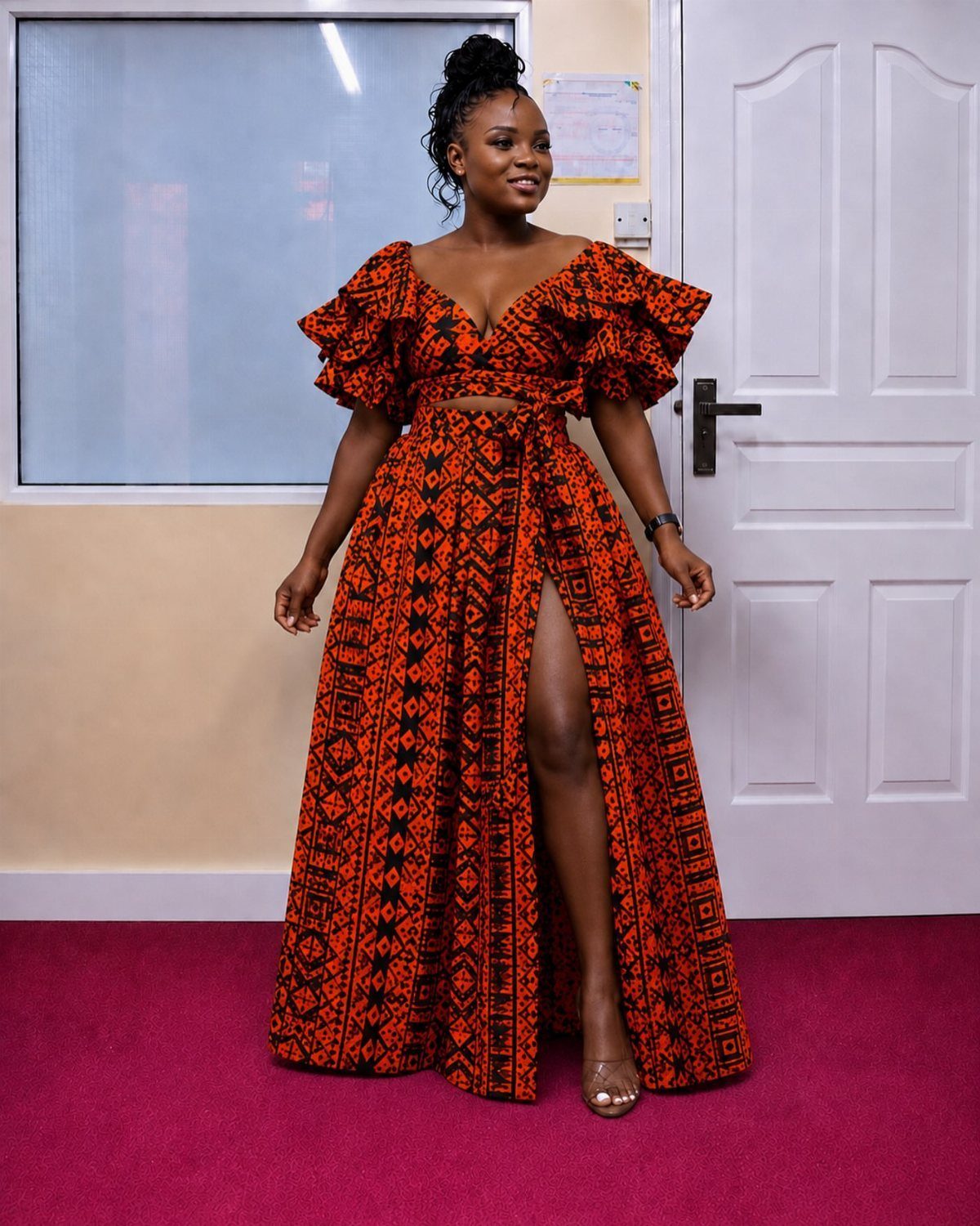 Woman posing in a vibrant orange and black patterned African print two-piece outfit.