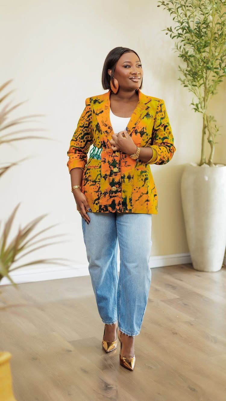 A woman posing in a vibrant yellow and orange patterned statement blazer and blue jeans.