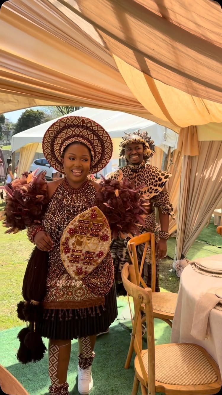 A woman wearing traditional Zulu clothing with a large beaded headdress and black pleated skirt.