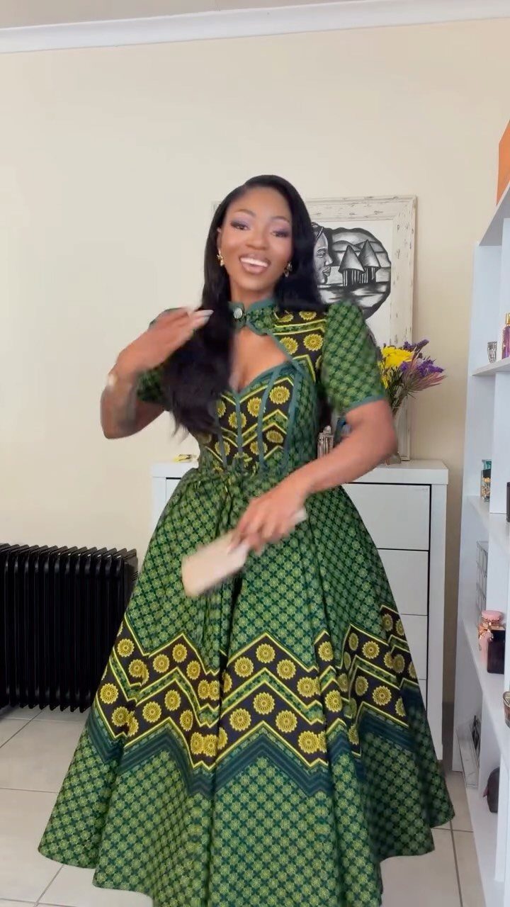 A woman smiling while wearing a green and yellow patterned African print maxi dress.