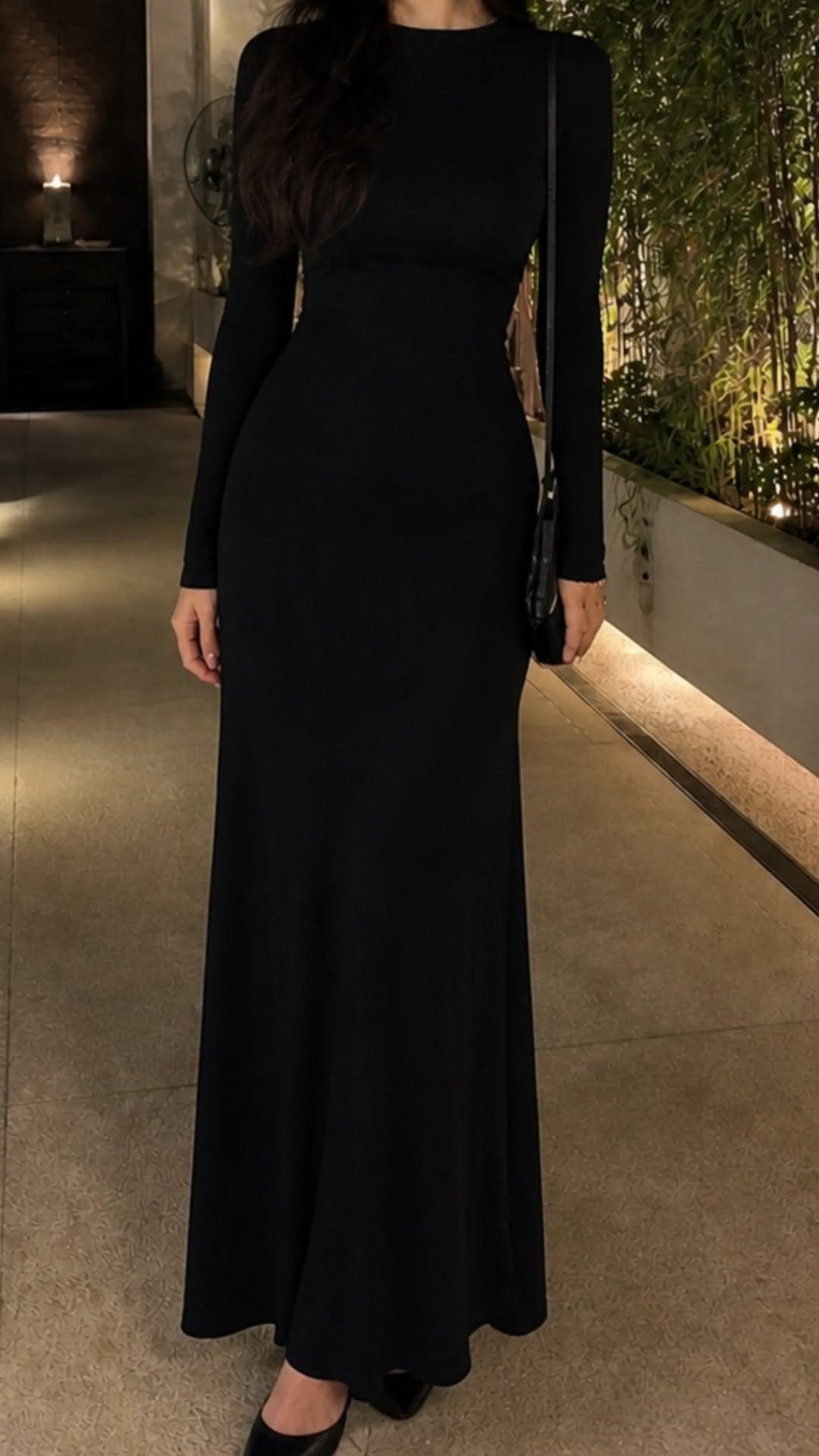 A person wearing a long-sleeved black bodycon maxi dress standing outdoors at night.