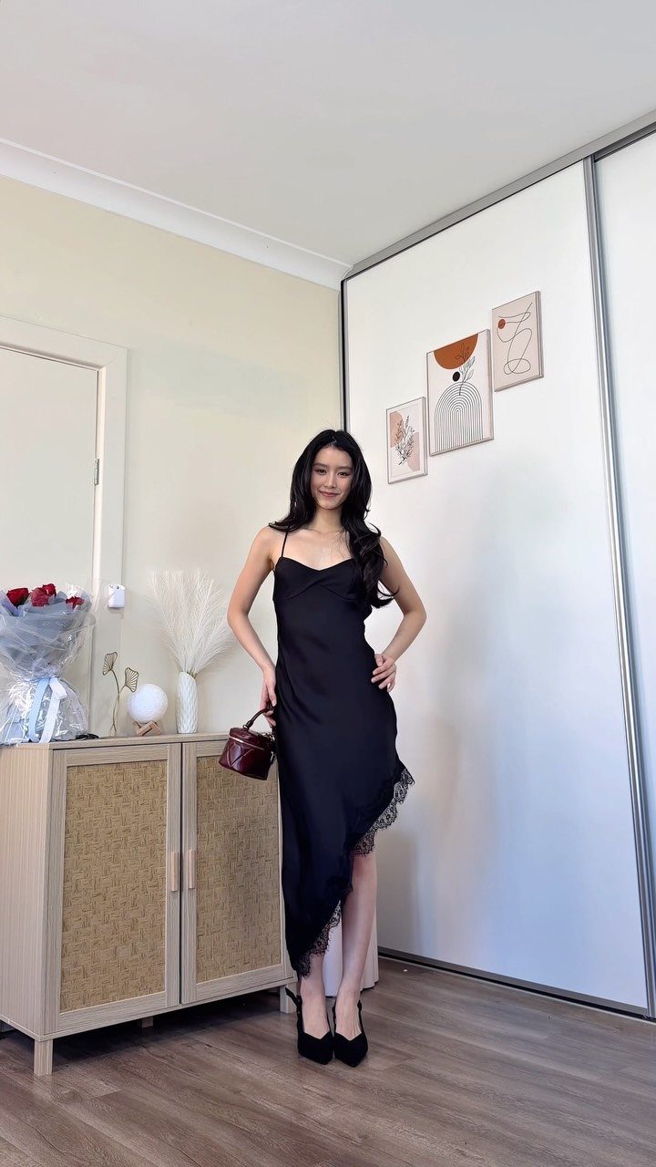A woman posing in a black satin midi slip dress with lace detailing.