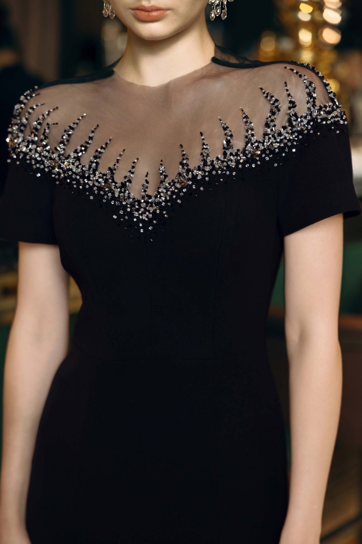 A person wearing a black dress with silver beaded embellishments on a sheer neckline.