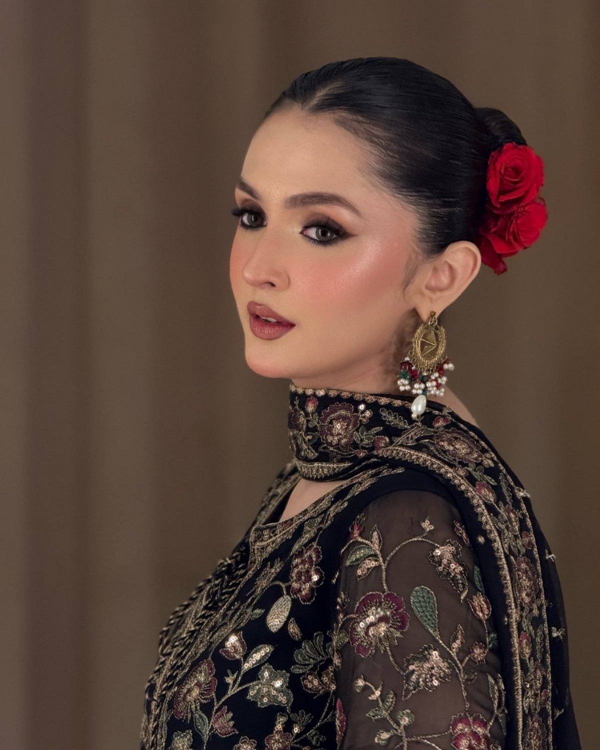 Woman with smoky eye makeup and red roses in her hair wearing an embroidered black dress.
