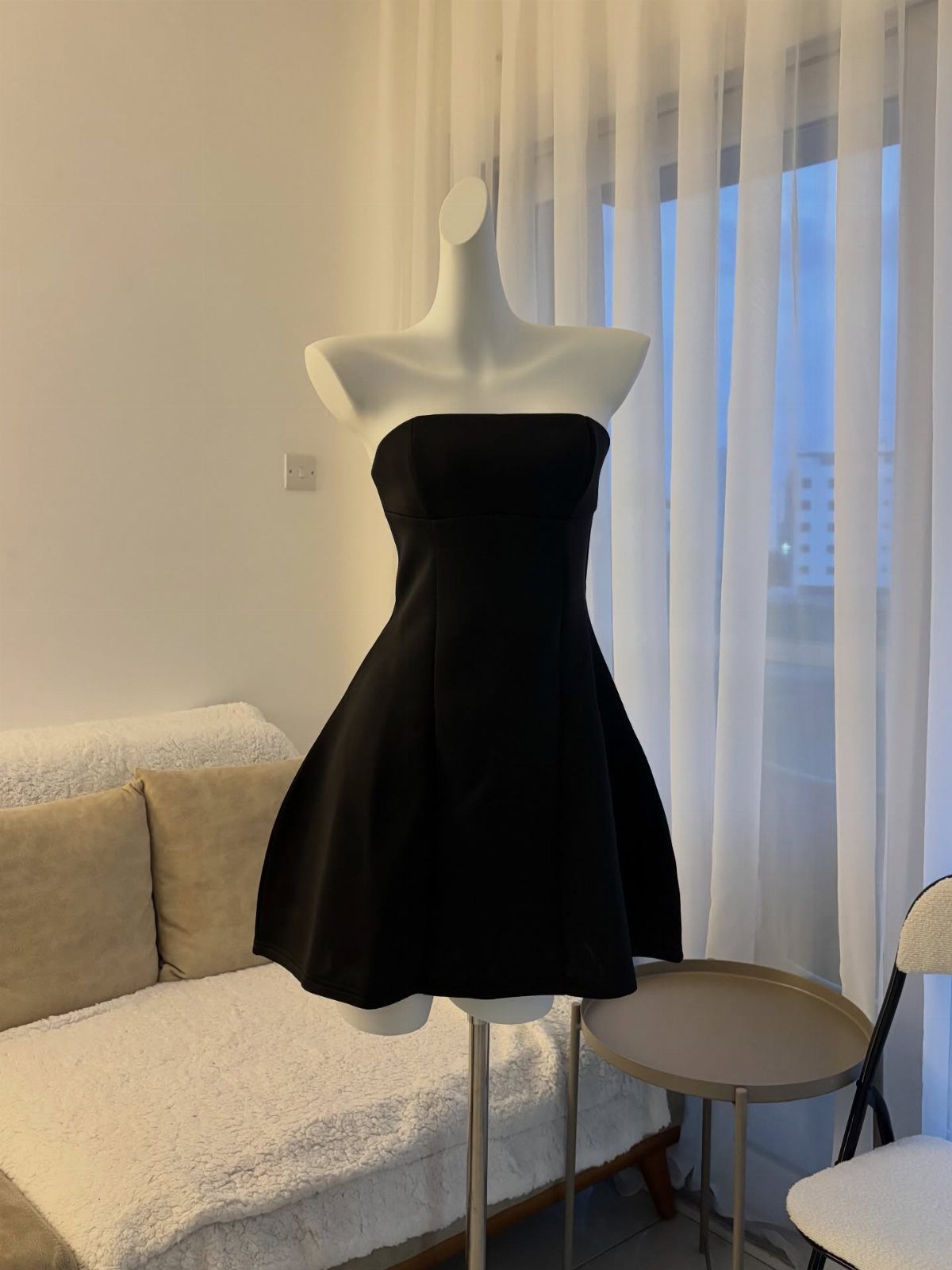 A black strapless flared dress displayed on a white mannequin in a bright room.