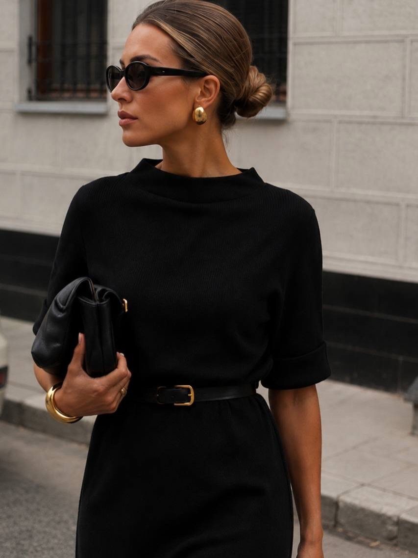 Woman in a black dress wearing a thin black belt with a gold buckle.