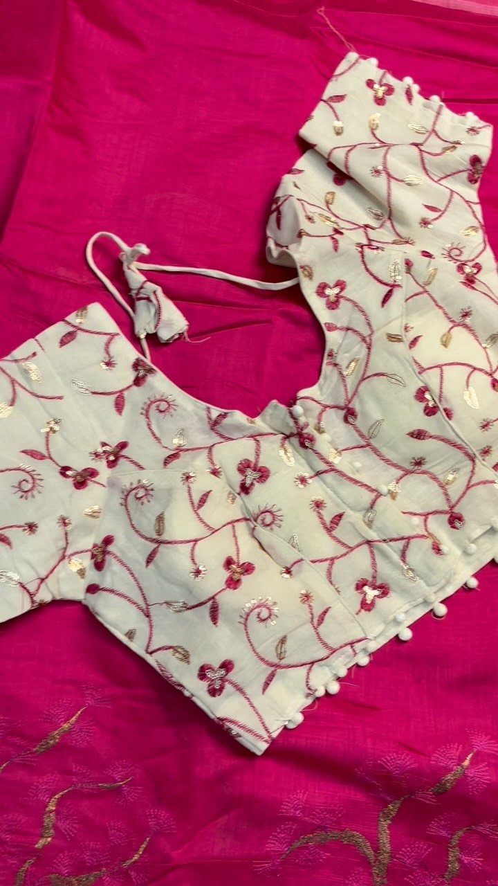 White blouse with pink floral embroidery and beadwork resting on bright pink fabric.
