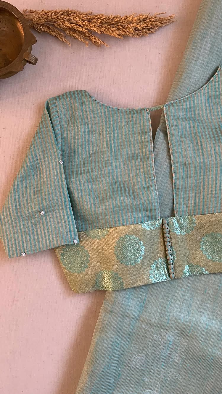 A sage green textured fabric blouse with a gold patterned waistband on a pink background.