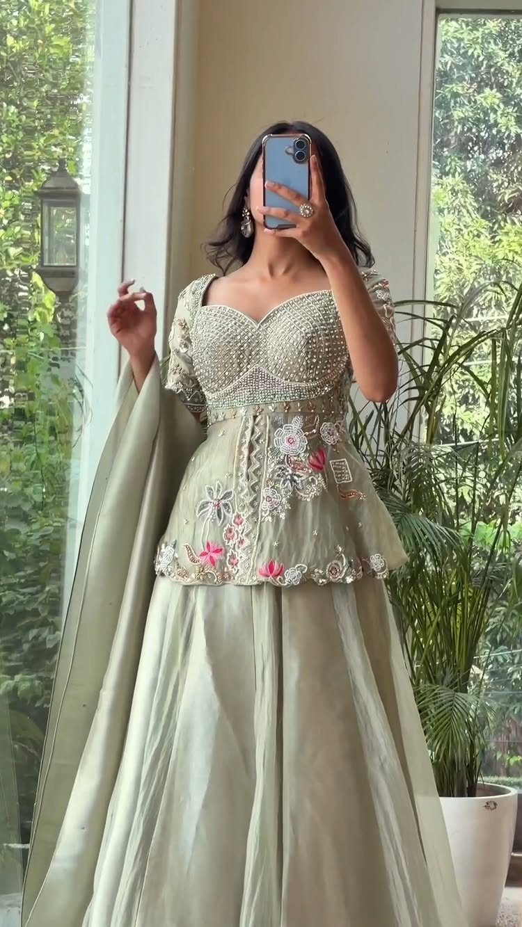 Woman in a sage green embroidered peplum blouse and matching long skirt posing for a selfie.