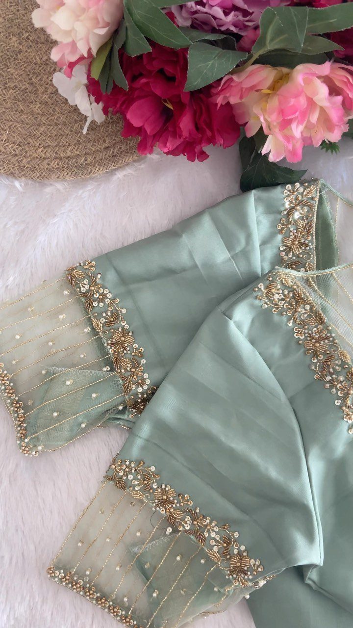 Sage green silk blouse with gold embroidered sheer sleeves resting near pink flowers.