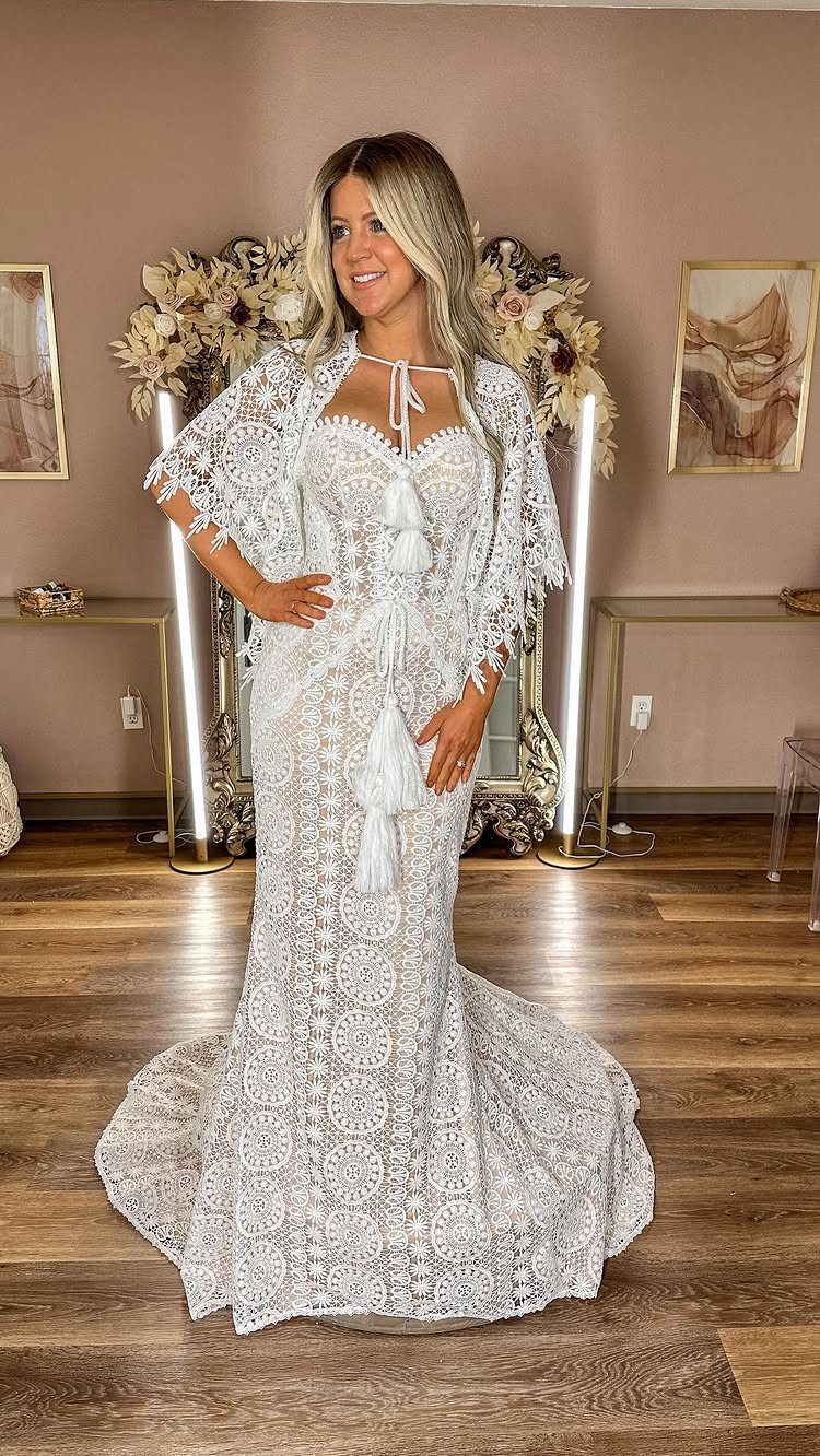 Woman wearing a white lace boho wedding dress with tassel details and flared sleeves.