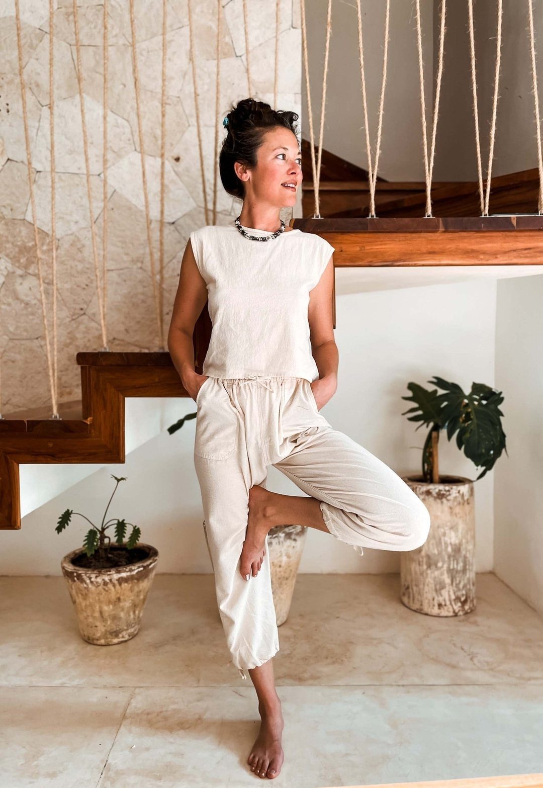 Woman in cream linen sleeveless top and loose trousers posing in a bright room.