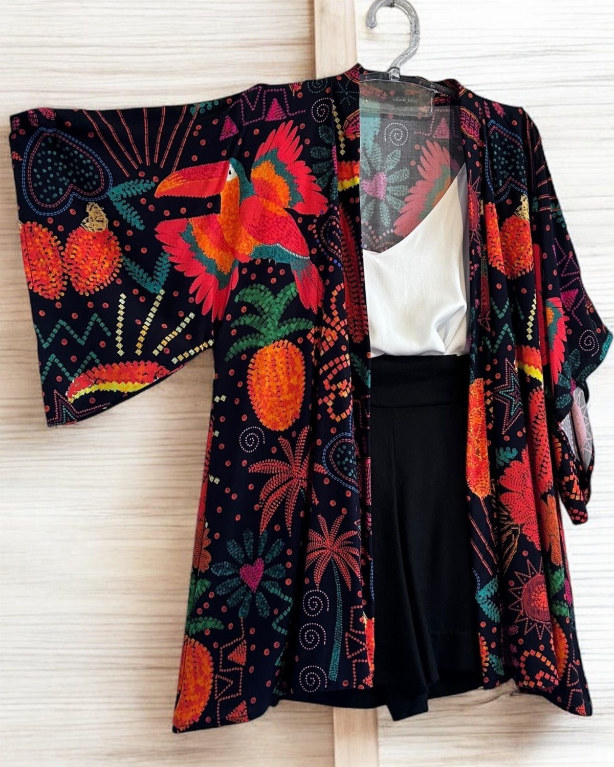 A black tropical patterned kimono hanging over a white top and black shorts.