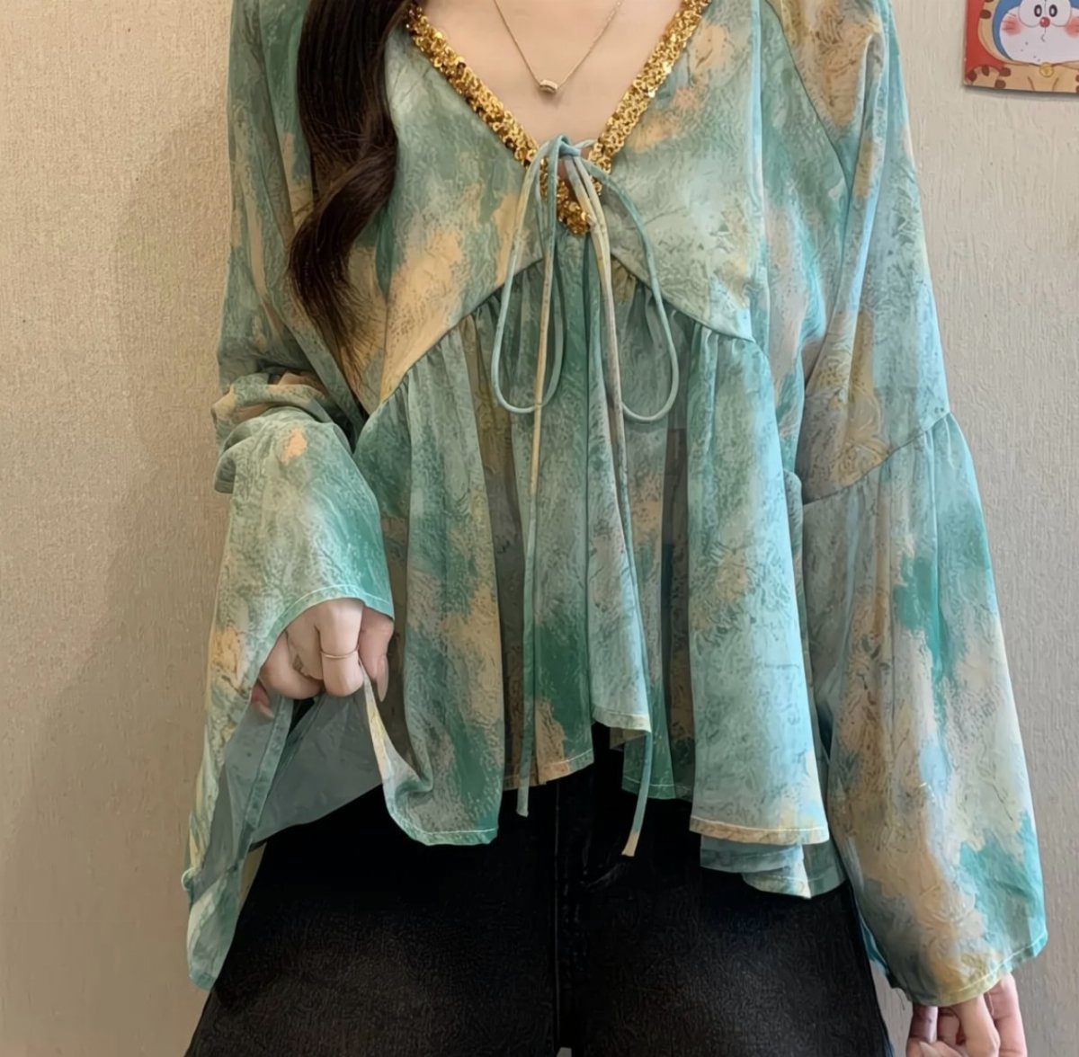 A person wearing a teal patterned peasant blouse with gold trim and bell sleeves.