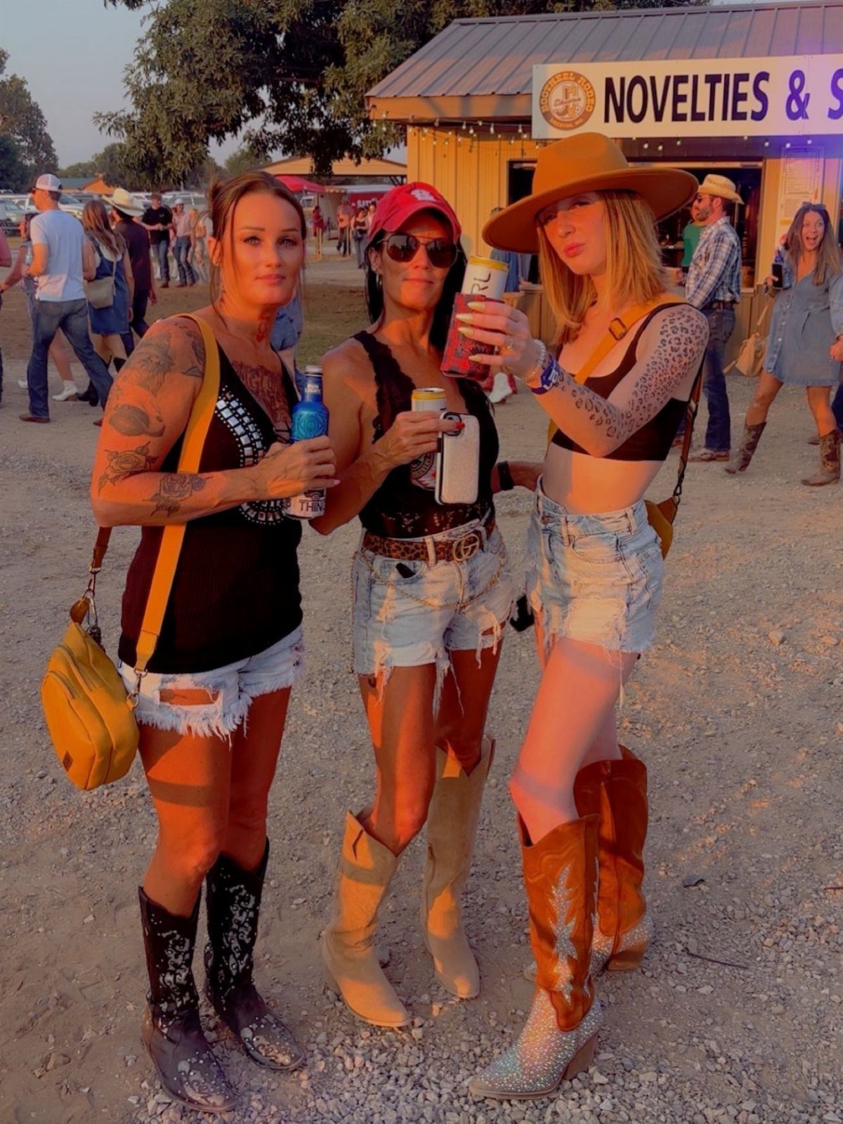 Three women posing outdoors wearing denim shorts, tank tops, and various styles of cowboy boots.