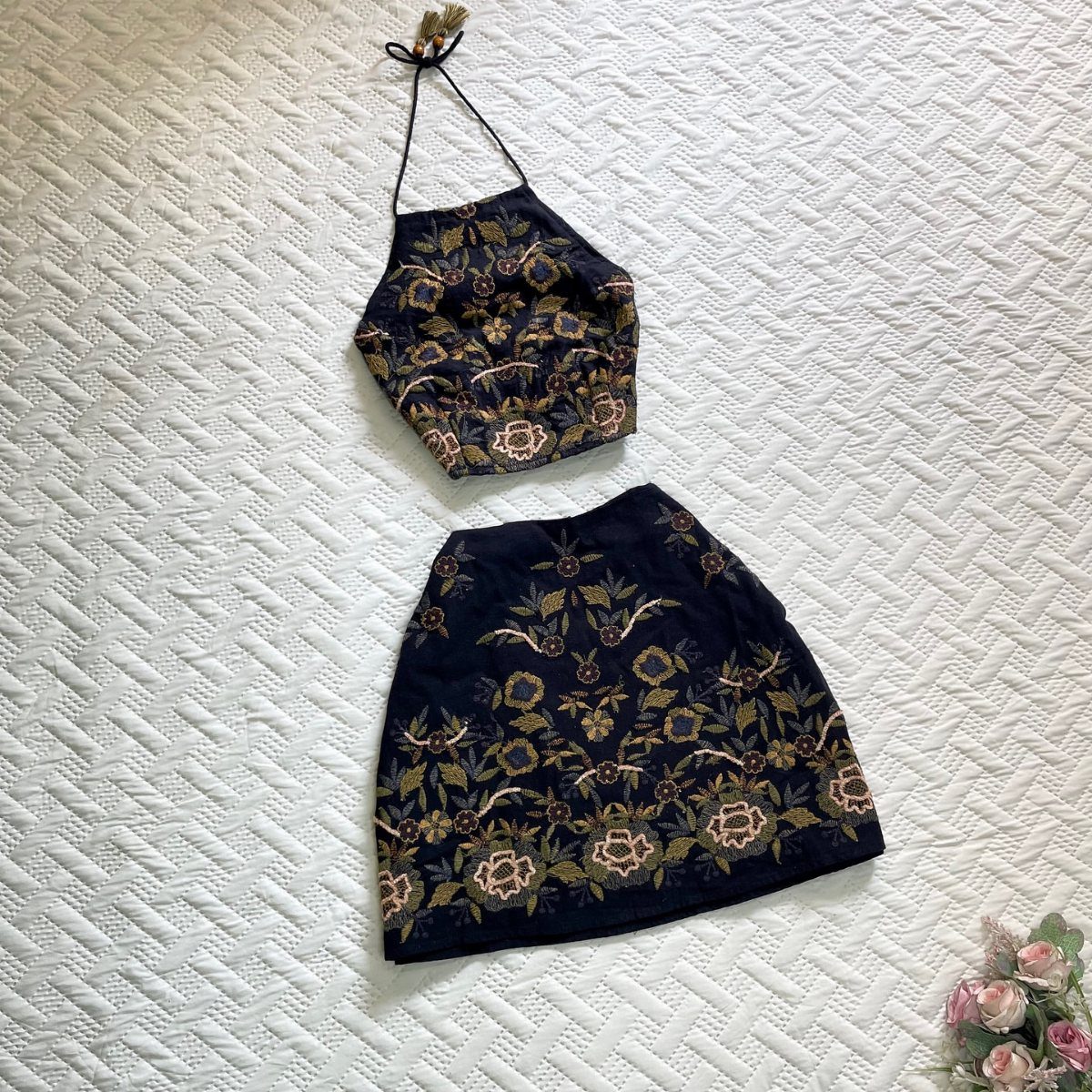 Black halter crop top and mini skirt with gold floral embroidery laid on white fabric.