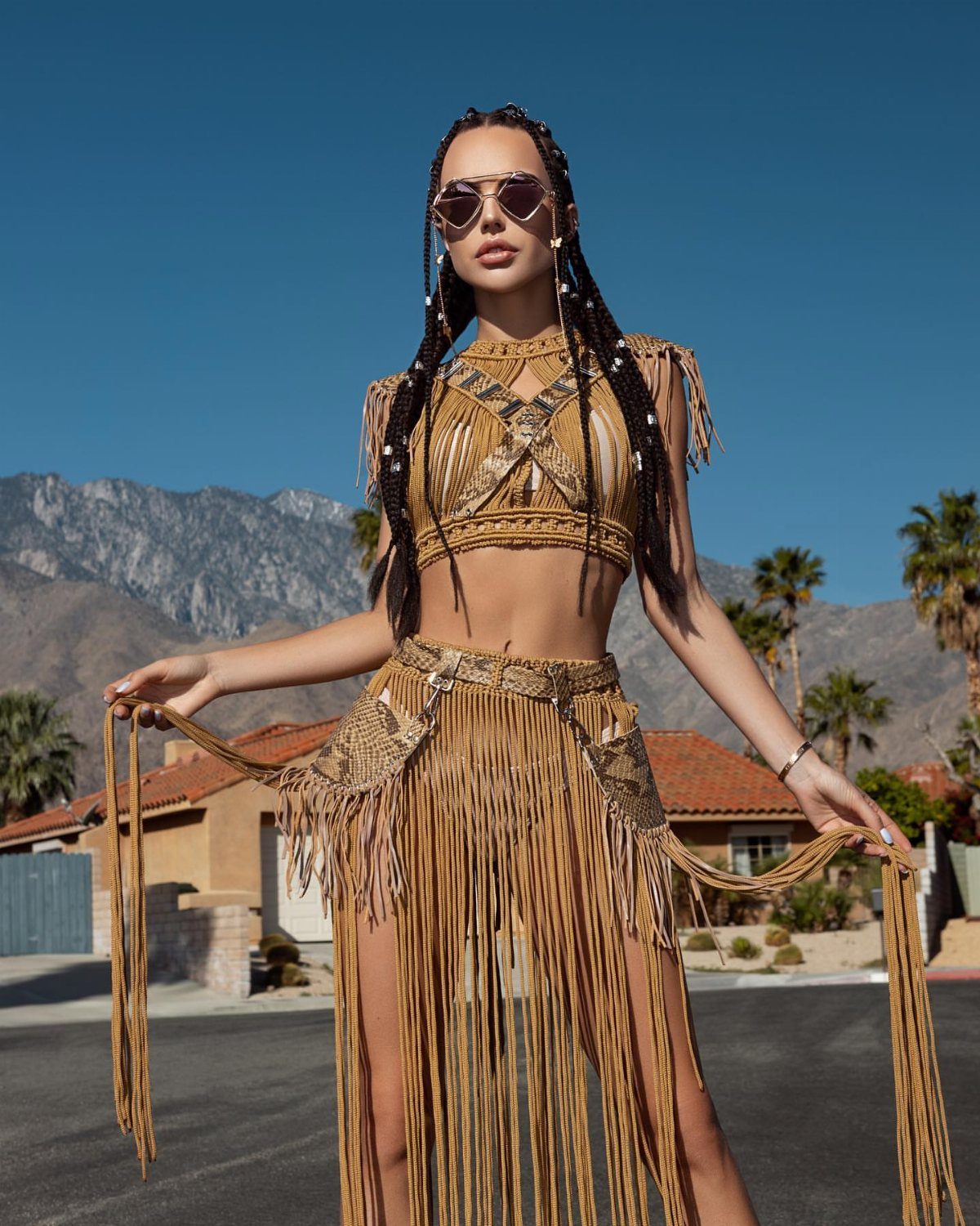 A woman posing in a tan crochet crop top and long fringe skirt outdoors.