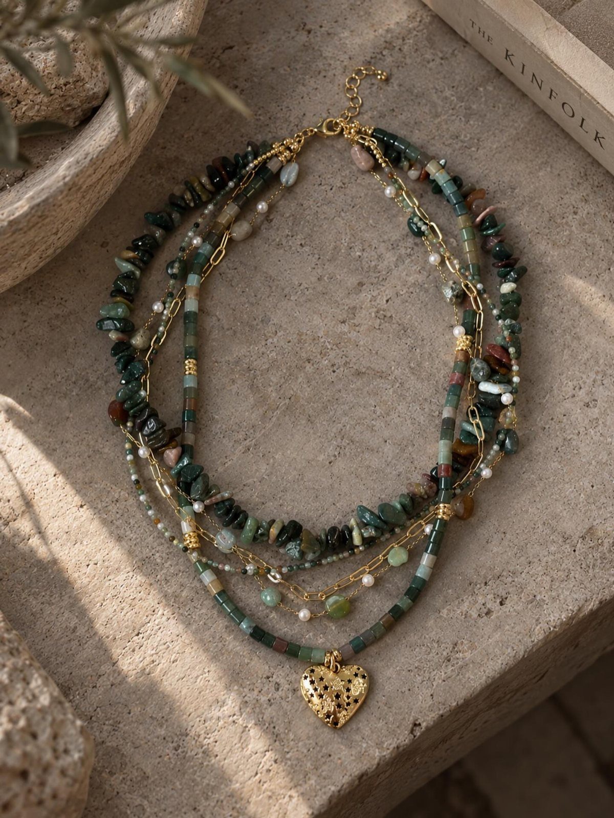 Layered beaded necklaces with a gold heart pendant resting on a stone surface.