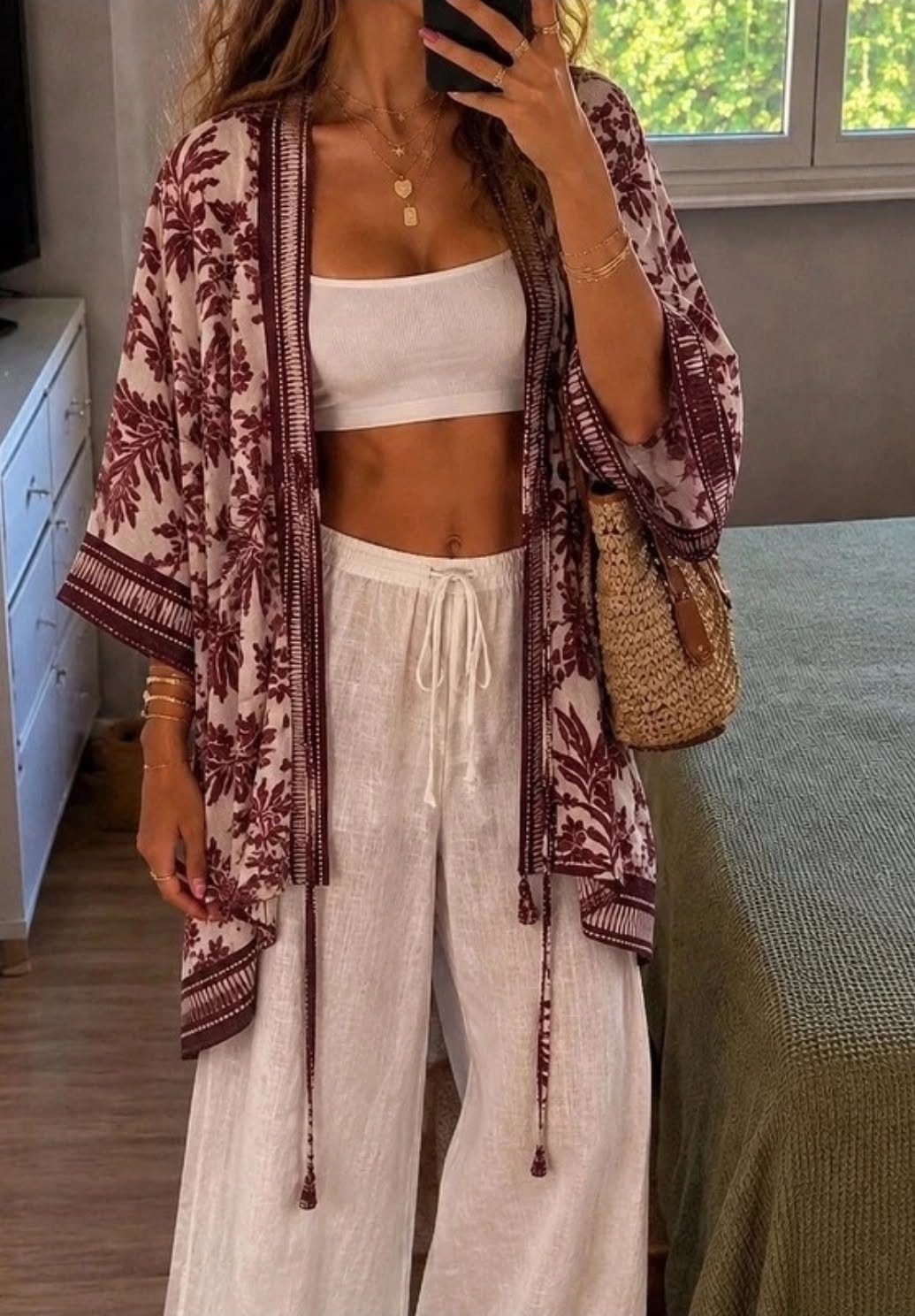 Woman wearing a white linen outfit with a patterned maroon kimono and straw bag.