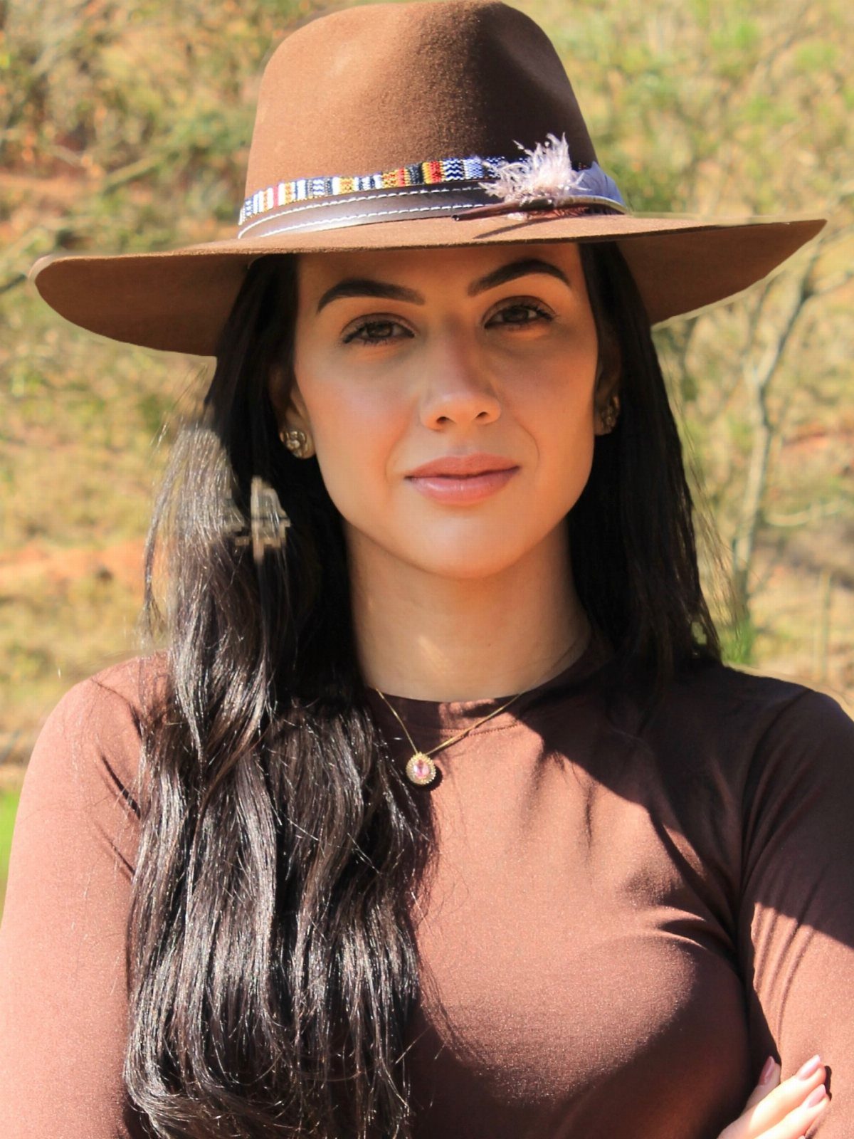 A woman wearing a brown wide-brimmed hat with a beaded band and feather decoration.
