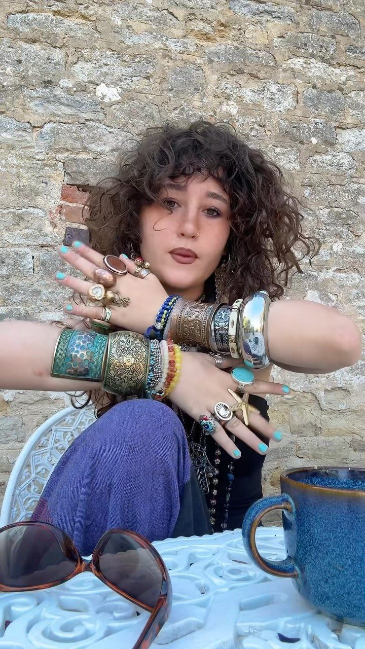 Woman displaying many large rings and stacked bracelets on her hands and wrists.