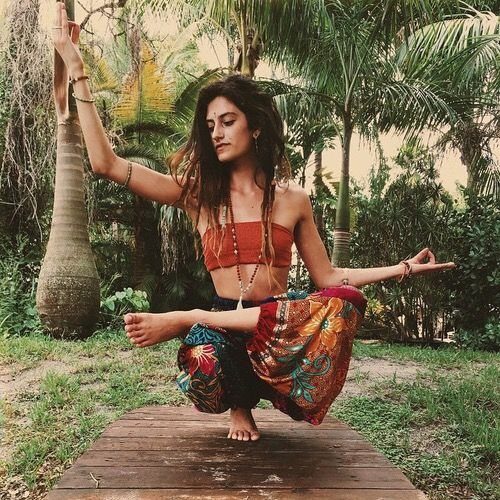 Woman in colorful patterned harem pants performing a yoga pose in a tropical garden.