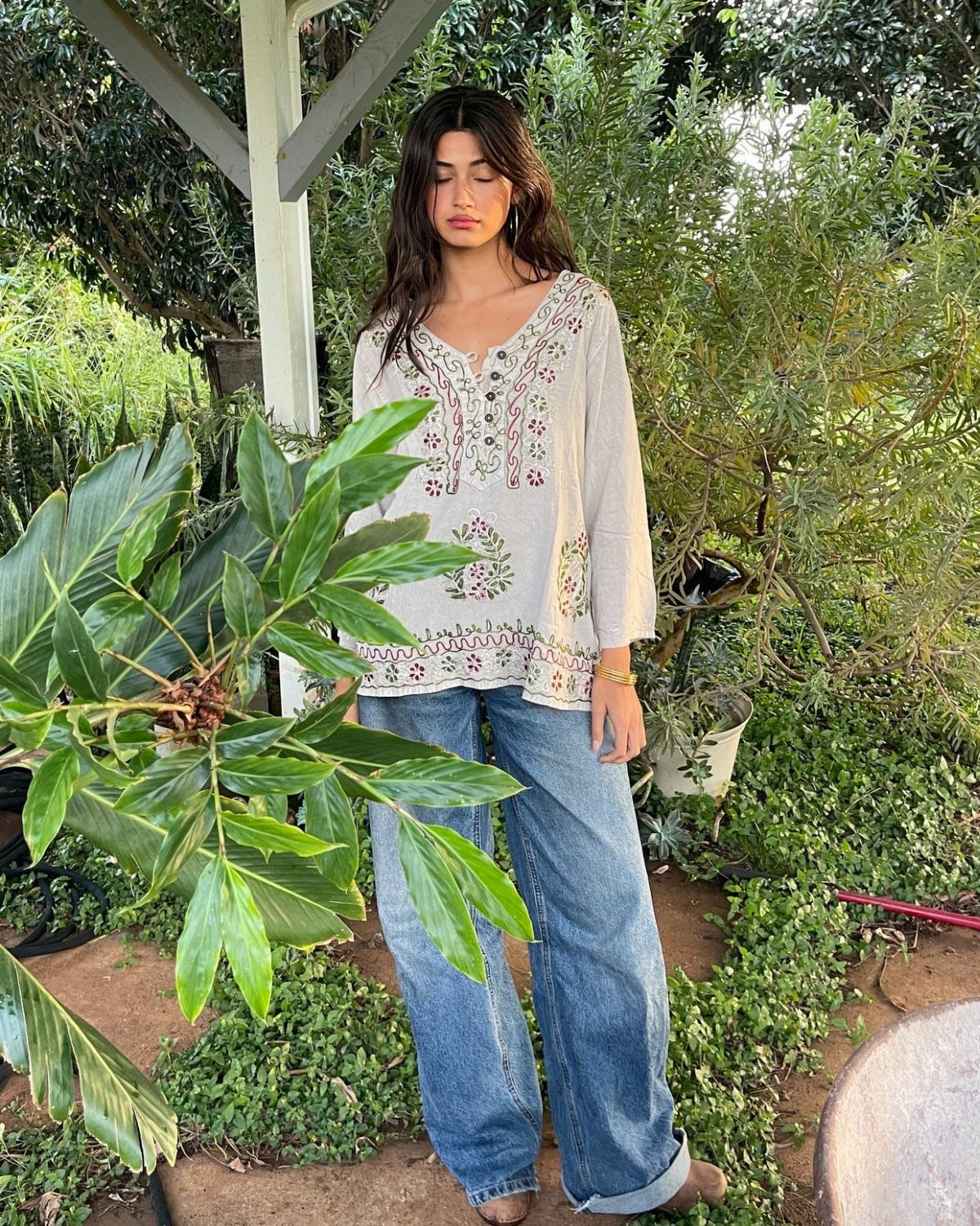 Woman wearing a cream floral print blouse and wide-leg denim jeans standing in a garden.