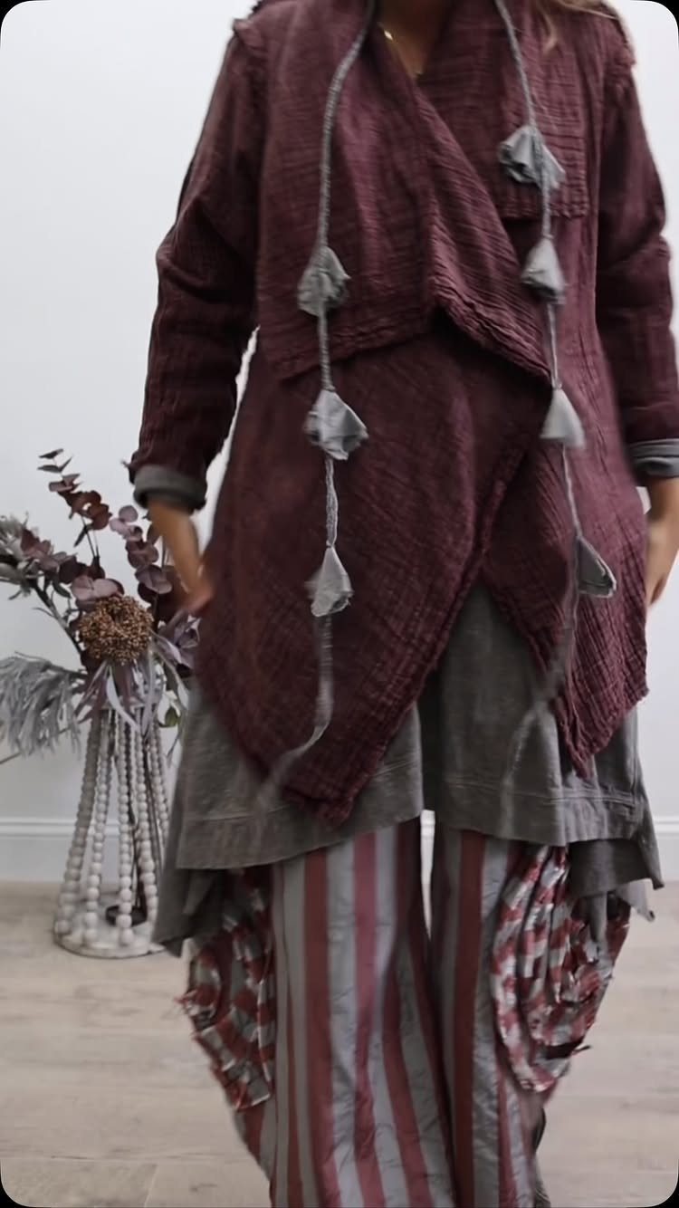 A person wearing layered maroon and grey bohemian textured clothing with striped trousers.