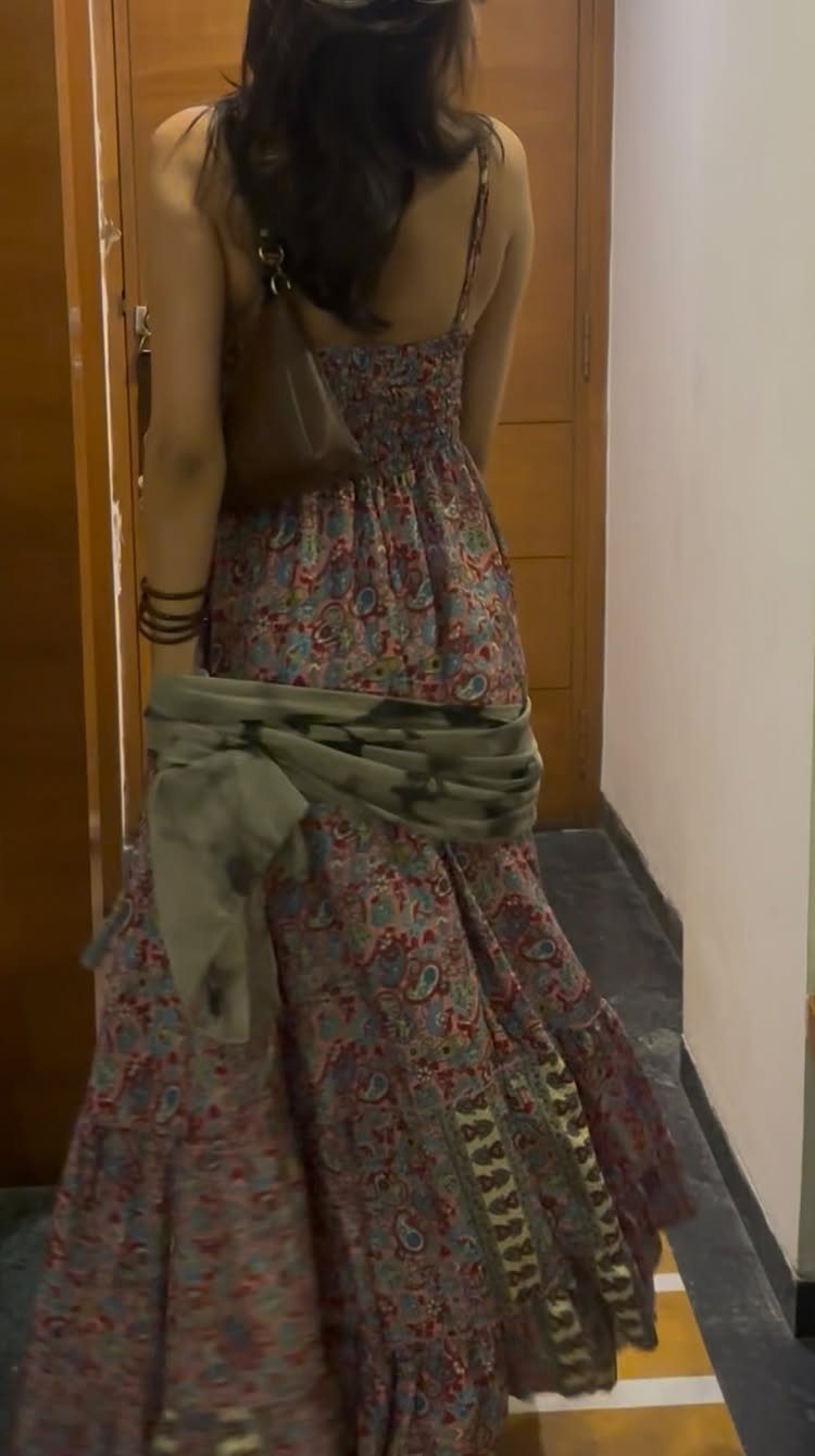 Woman wearing a long floral print maxi dress with a green fabric tied around her waist.