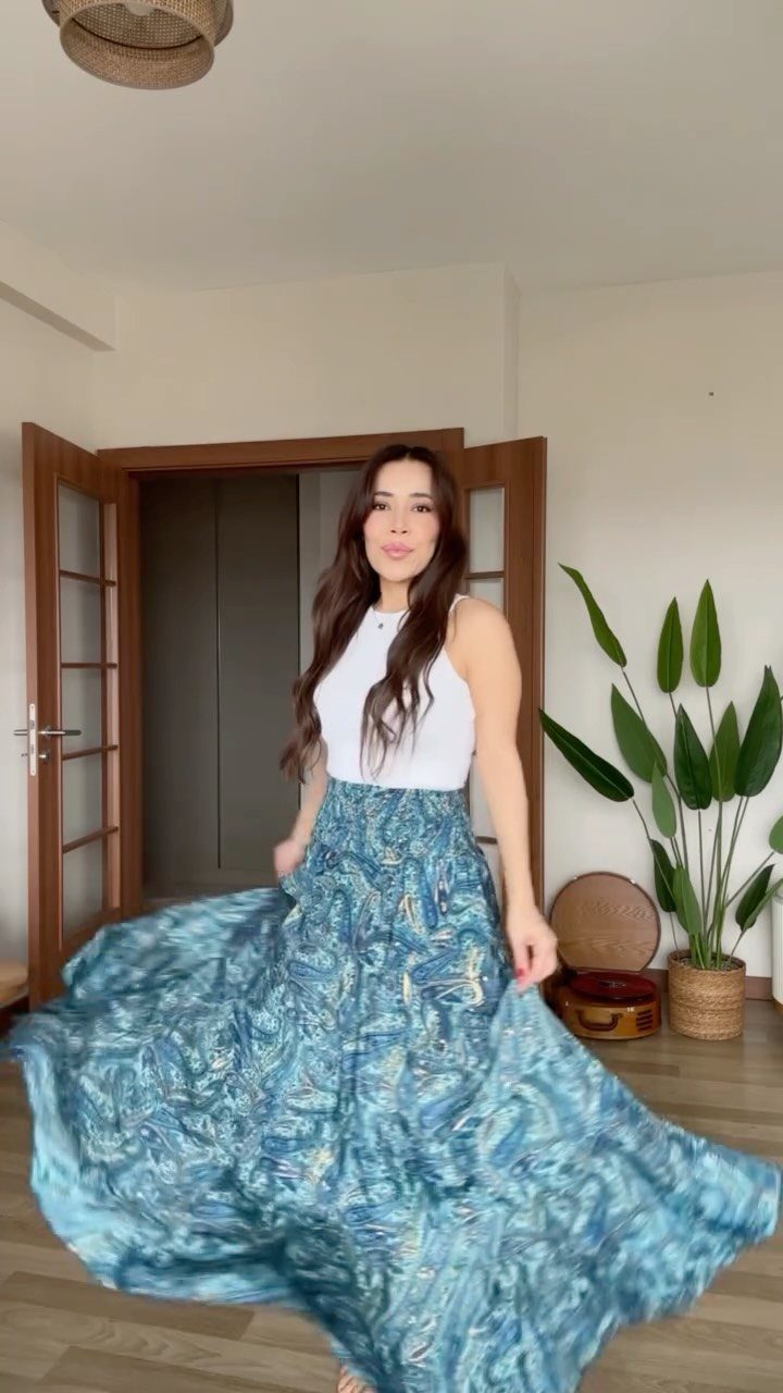 A woman twirling in a long, blue patterned maxi skirt and white halter top.