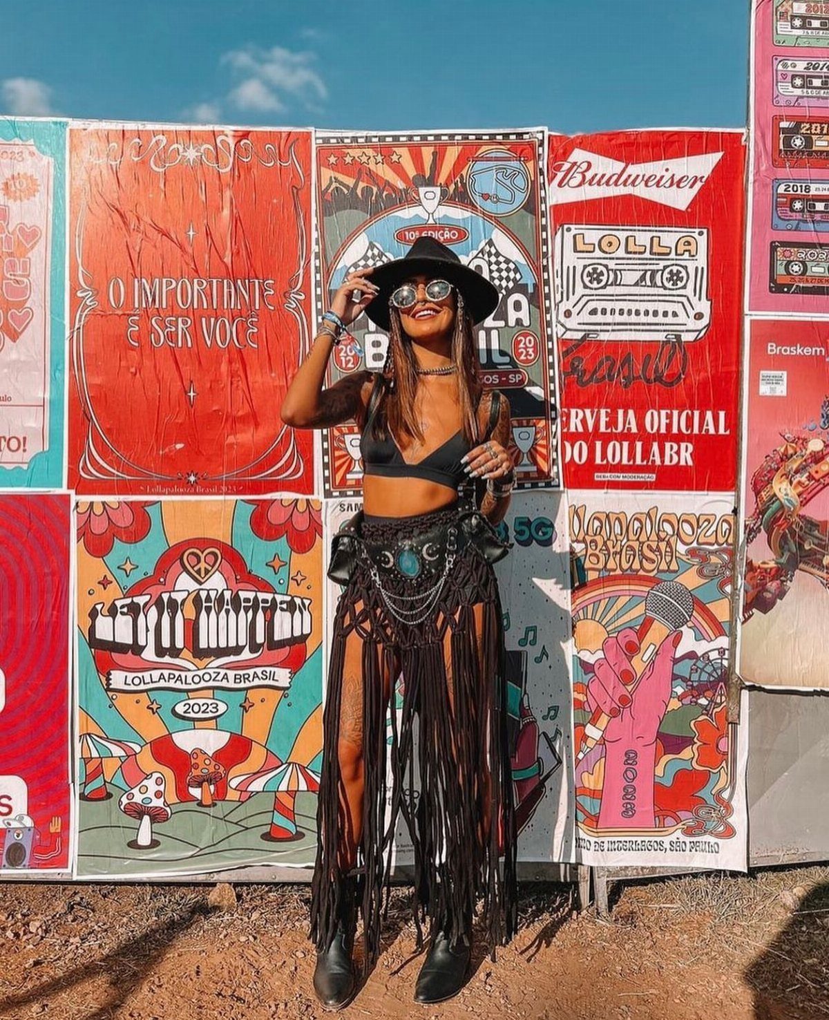 Woman in black festival attire and fringed skirt posing in front of colorful posters.