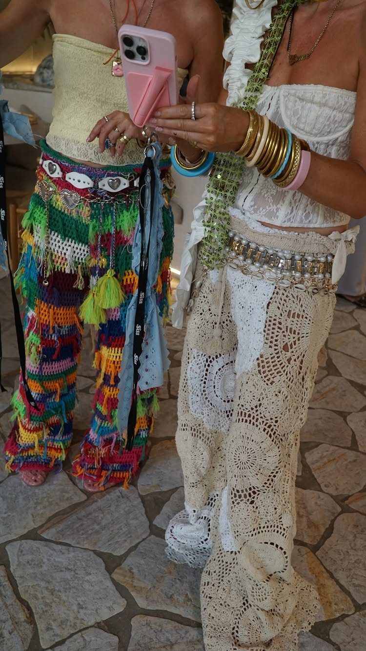 Two people wearing colorful crochet bohemian style pants and tops standing on stone tiles.