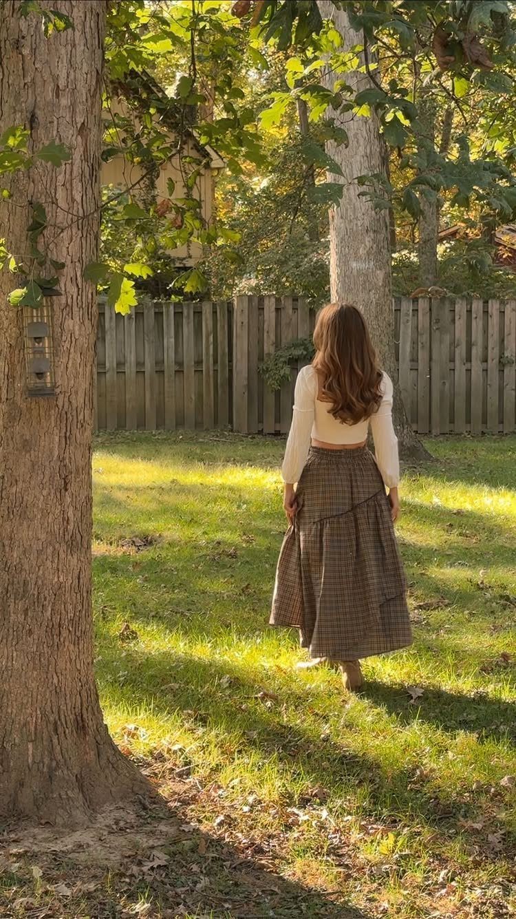 Woman in a long patterned maxi skirt standing in a sunny backyard with trees.