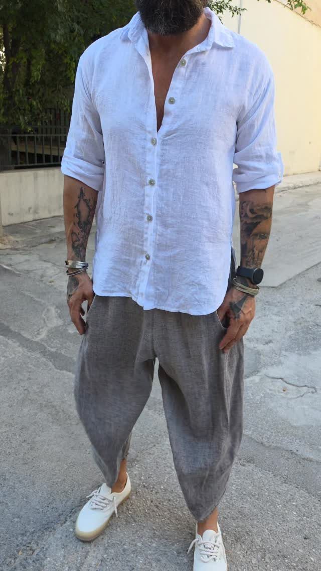 Man wearing a white linen shirt, grey harem pants, and white sneakers standing on a street.
