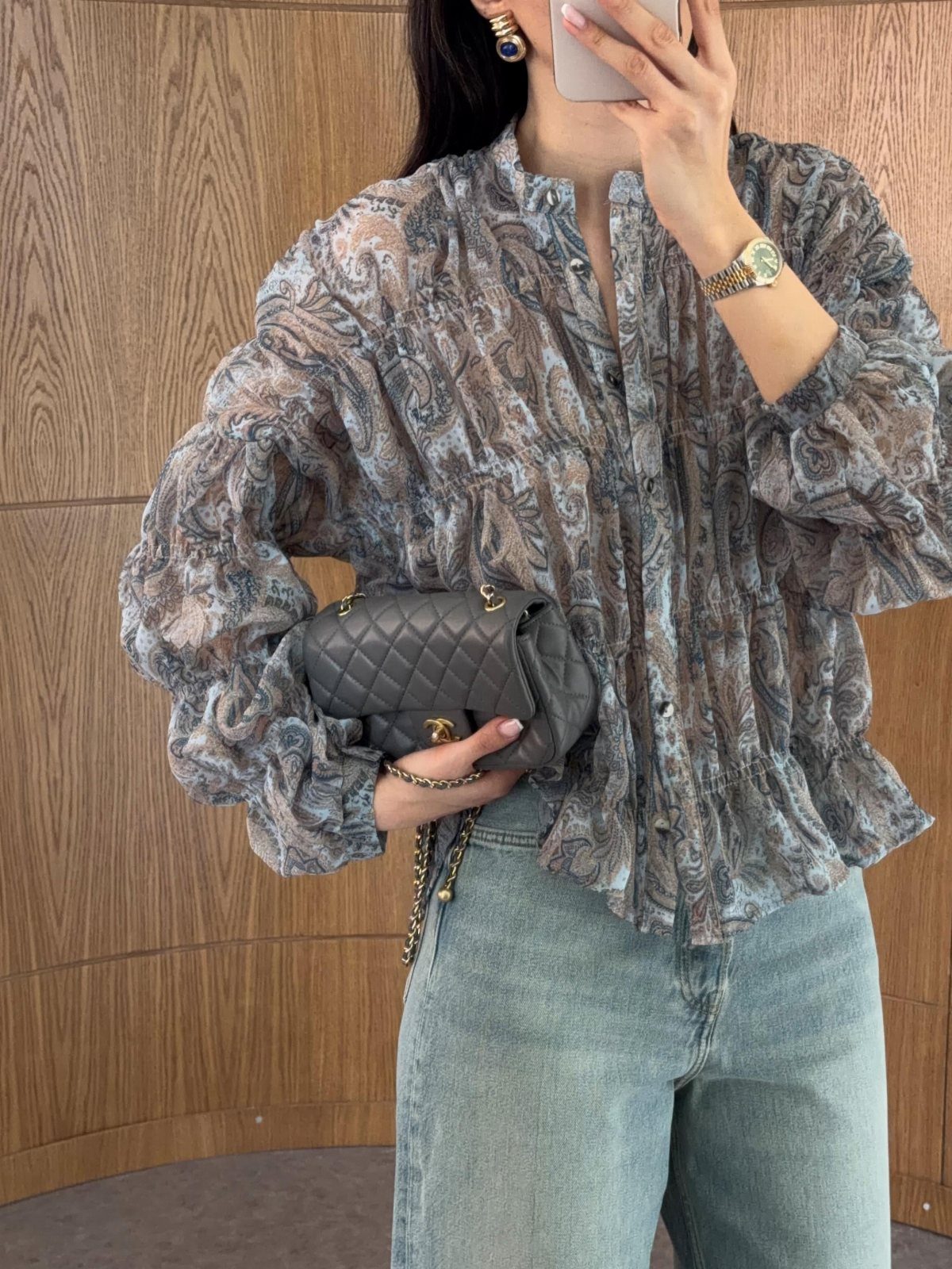 A person wearing a patterned peasant blouse with voluminous sleeves and light blue denim jeans.